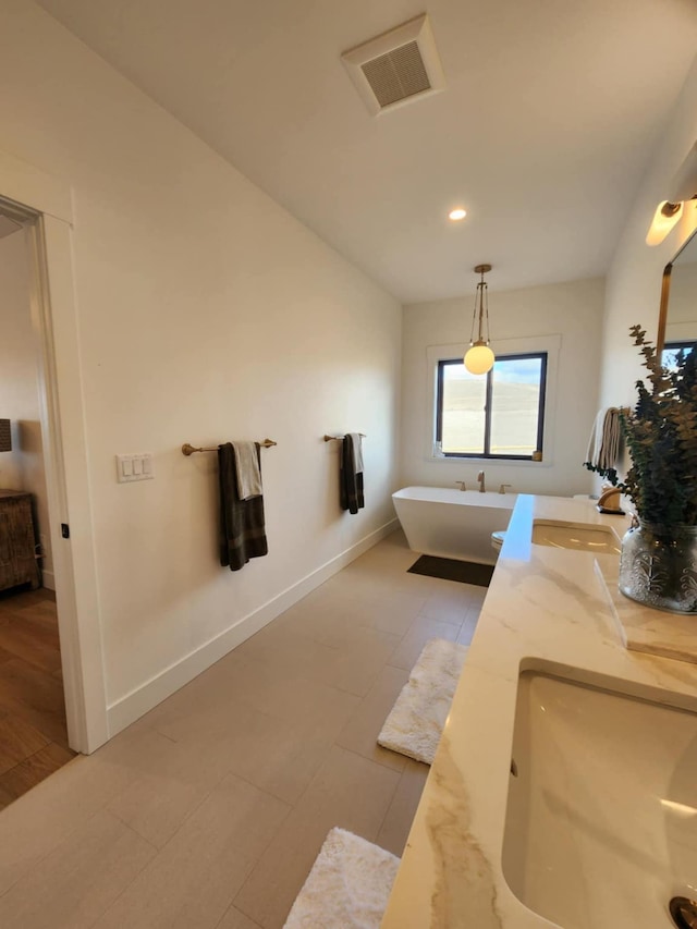 full bathroom featuring visible vents, a sink, a freestanding bath, and double vanity