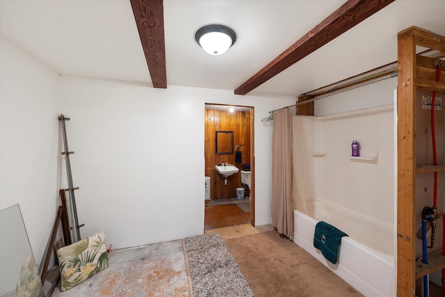 bathroom featuring beam ceiling, shower / bath combo with shower curtain, and sink