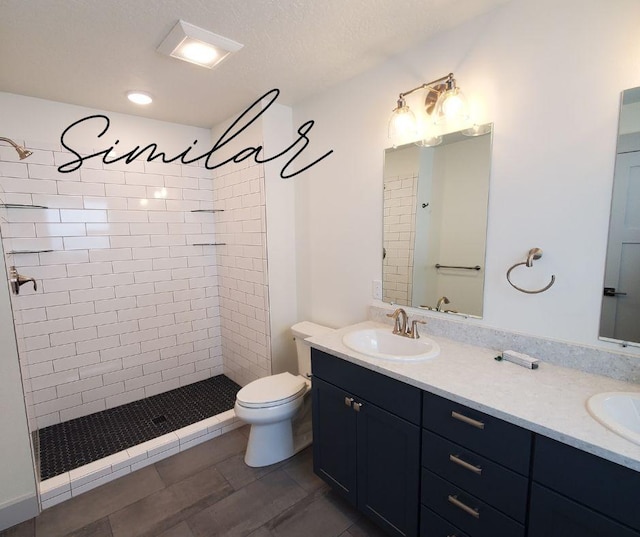 bathroom with toilet, a textured ceiling, tiled shower, wood-type flooring, and vanity