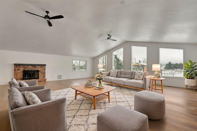 living room with a fireplace, light wood-type flooring, vaulted ceiling, and ceiling fan