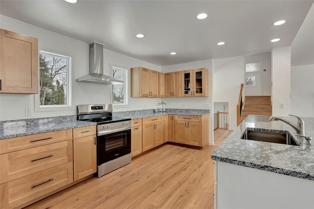 kitchen with light stone counters, stainless steel range oven, wall chimney range hood, and sink