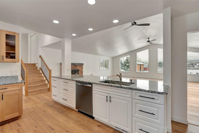 kitchen with light stone countertops, dishwasher, sink, vaulted ceiling, and white cabinets