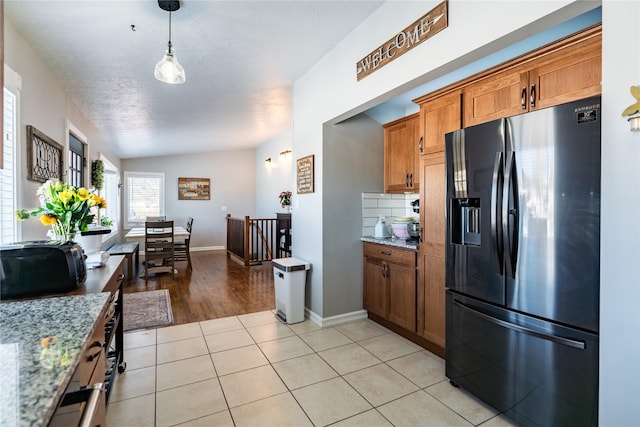 kitchen with stainless steel refrigerator with ice dispenser, light stone counters, vaulted ceiling, pendant lighting, and light tile patterned flooring