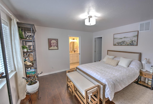 bedroom with dark wood-style flooring, connected bathroom, visible vents, and baseboards