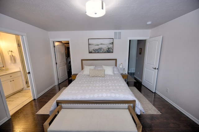 bedroom with baseboards, visible vents, dark wood-type flooring, ensuite bathroom, and a textured ceiling