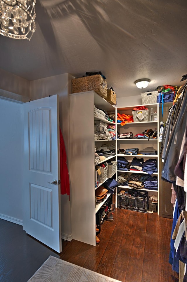 walk in closet featuring dark wood finished floors and an inviting chandelier