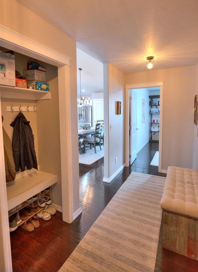 corridor featuring a notable chandelier, dark wood finished floors, and baseboards