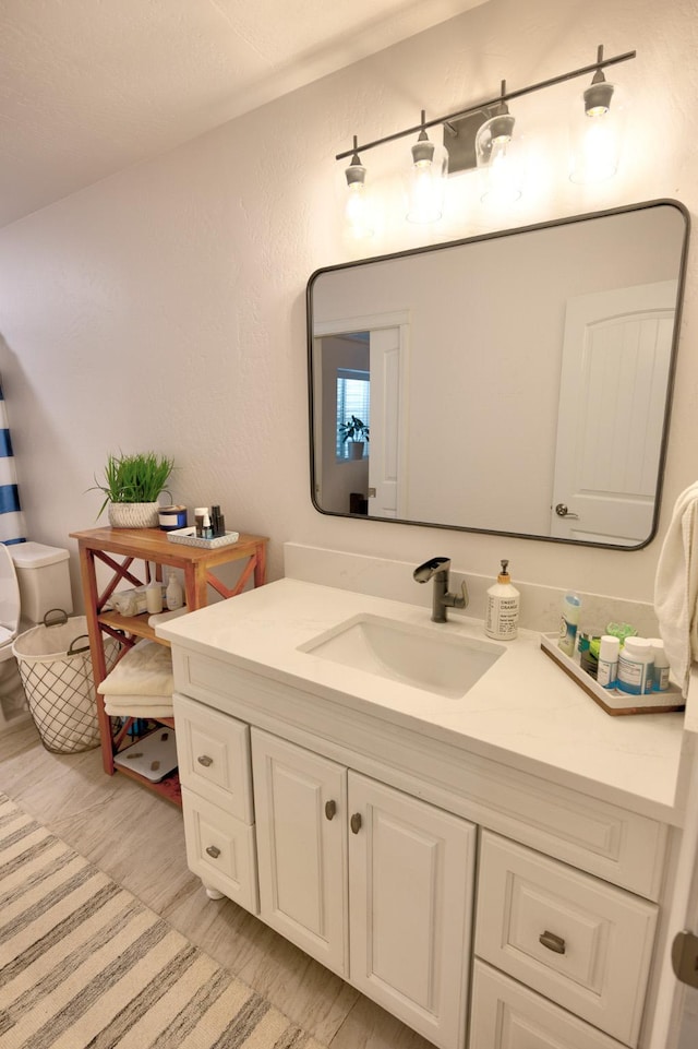 bathroom featuring toilet, a textured wall, and vanity