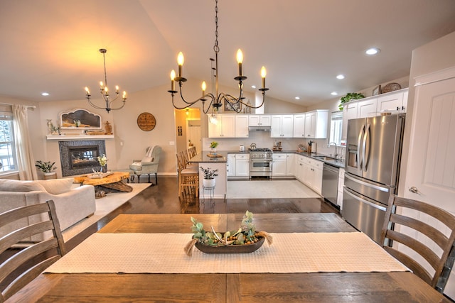 dining room with recessed lighting, vaulted ceiling, dark wood-style floors, a glass covered fireplace, and an inviting chandelier