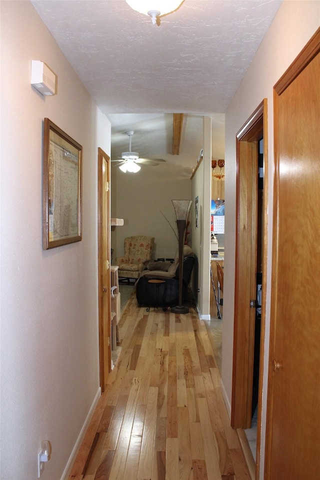 hall with beam ceiling, a textured ceiling, and light hardwood / wood-style flooring