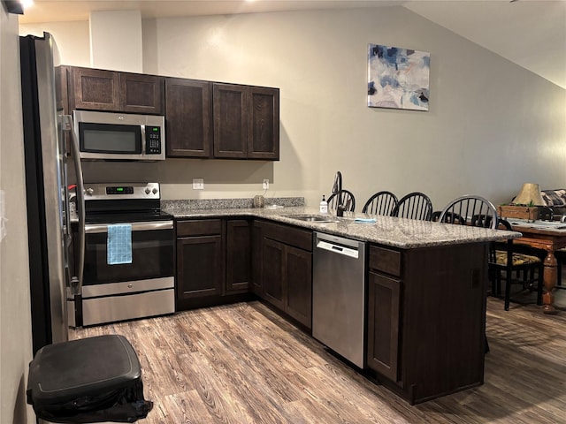 kitchen featuring kitchen peninsula, appliances with stainless steel finishes, light wood-type flooring, and lofted ceiling