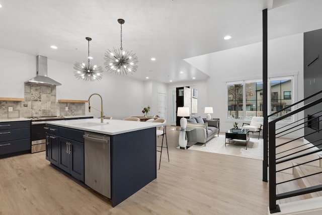 kitchen featuring sink, wall chimney exhaust hood, hanging light fixtures, an island with sink, and appliances with stainless steel finishes