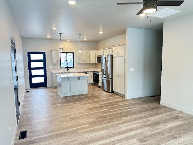 kitchen with appliances with stainless steel finishes, a kitchen island, ceiling fan, pendant lighting, and white cabinetry