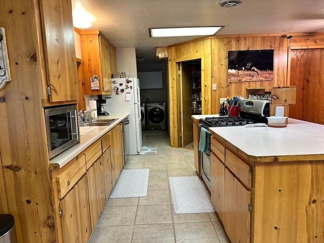 kitchen featuring sink, independent washer and dryer, wooden walls, light tile patterned flooring, and appliances with stainless steel finishes