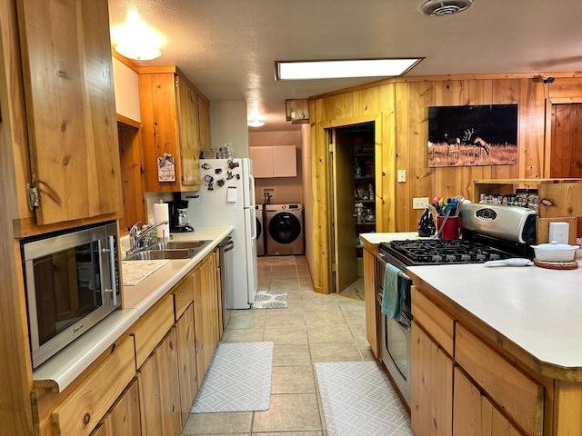 kitchen featuring sink, wooden walls, independent washer and dryer, a textured ceiling, and stainless steel appliances