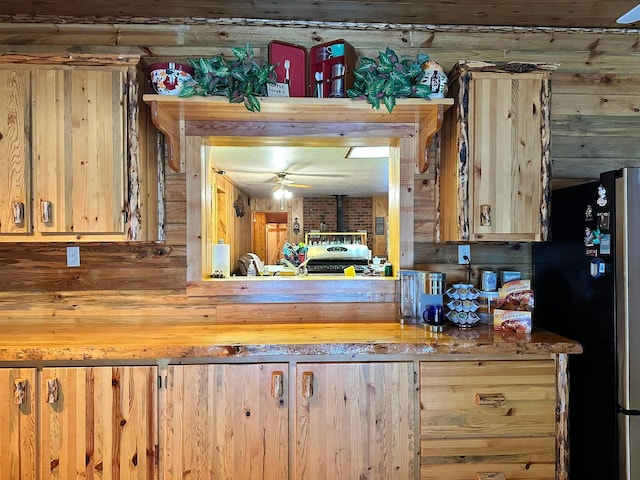 kitchen featuring stainless steel refrigerator, ceiling fan, and wooden walls