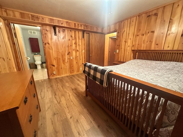 bedroom featuring connected bathroom, wood walls, and light hardwood / wood-style flooring