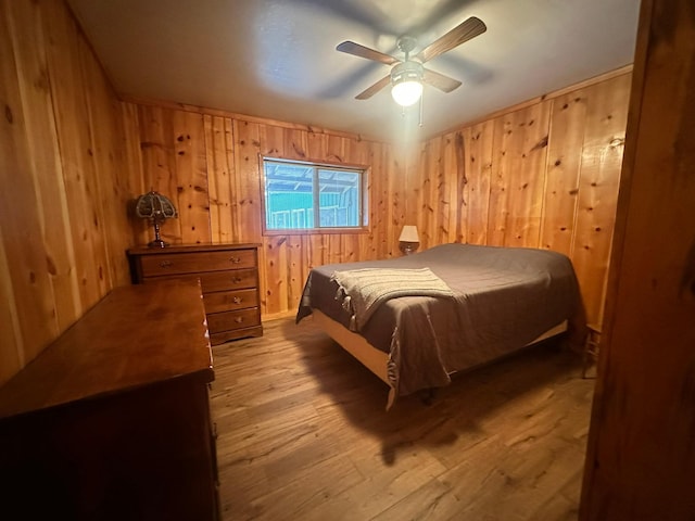 bedroom featuring hardwood / wood-style flooring, ceiling fan, and wood walls