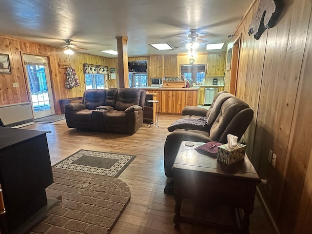 living room with light wood-type flooring, ceiling fan, and wooden walls