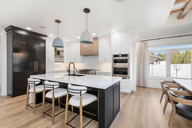 kitchen featuring double oven, sink, pendant lighting, a center island with sink, and built in refrigerator