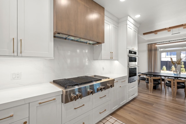 kitchen featuring light stone countertops, stainless steel appliances, decorative backsplash, white cabinets, and light wood-type flooring