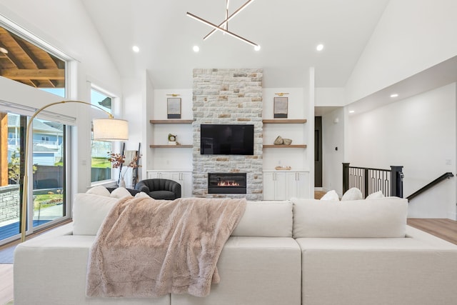 living room with built in shelves, light hardwood / wood-style flooring, high vaulted ceiling, a notable chandelier, and a fireplace