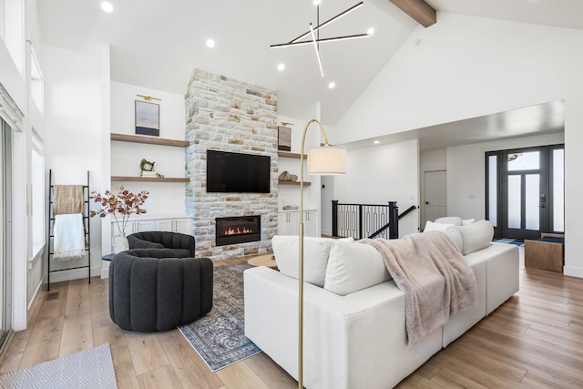 living room featuring high vaulted ceiling, a stone fireplace, light hardwood / wood-style floors, a notable chandelier, and beam ceiling