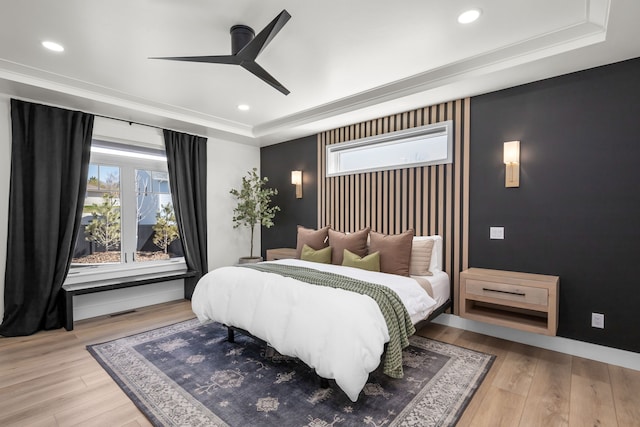 bedroom featuring light wood-type flooring, a raised ceiling, ceiling fan, and ornamental molding