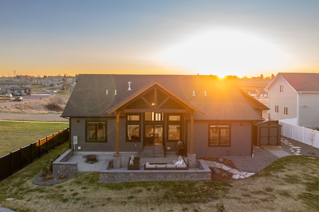 back house at dusk featuring a lawn, an outdoor living space, a shed, and a patio