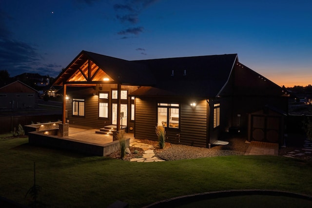 back house at dusk featuring a lawn and a storage shed