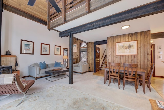 dining space with wood walls, beam ceiling, a wood stove, and light carpet