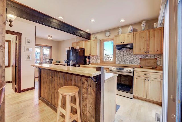 kitchen with stainless steel electric range oven, a kitchen island with sink, light hardwood / wood-style flooring, decorative backsplash, and black refrigerator