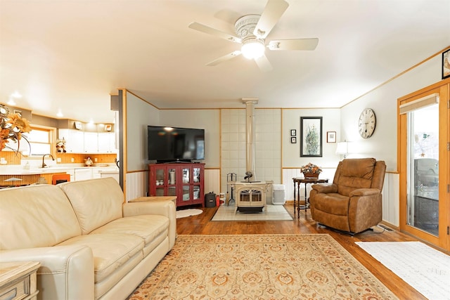 living room with light hardwood / wood-style floors, a wood stove, ceiling fan, and sink