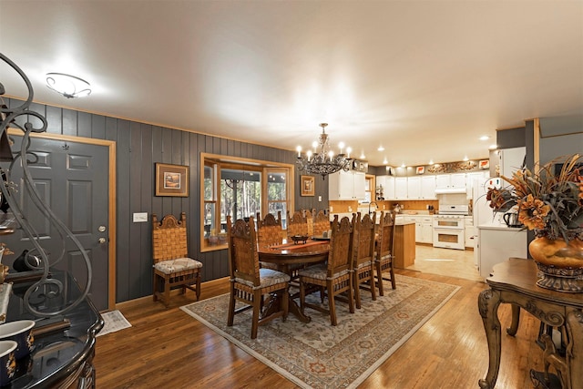 dining area featuring wooden walls, a chandelier, and light wood-type flooring