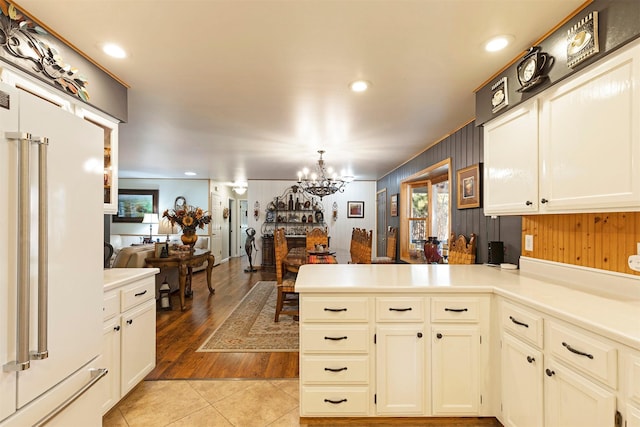 kitchen featuring kitchen peninsula, light tile patterned flooring, high end white refrigerator, a notable chandelier, and wood walls