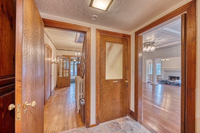 corridor with a textured ceiling, decorative columns, and ornamental molding