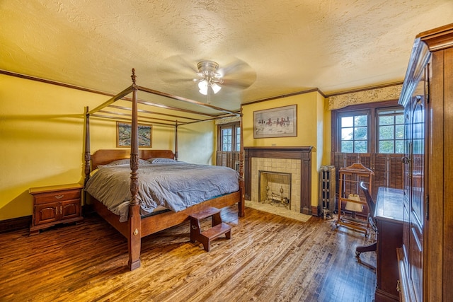 bedroom featuring ornamental molding, a textured ceiling, ceiling fan, a tile fireplace, and wood-type flooring