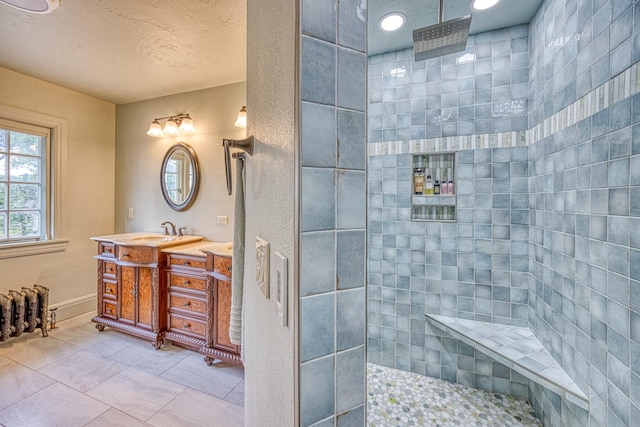 bathroom featuring tile patterned flooring, vanity, a tile shower, and a textured ceiling