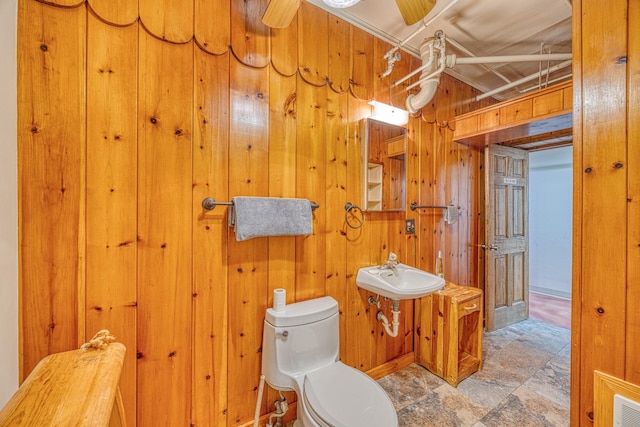 bathroom featuring ceiling fan, toilet, sink, and wooden walls