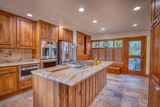 kitchen with decorative backsplash, light stone countertops, a center island, and appliances with stainless steel finishes