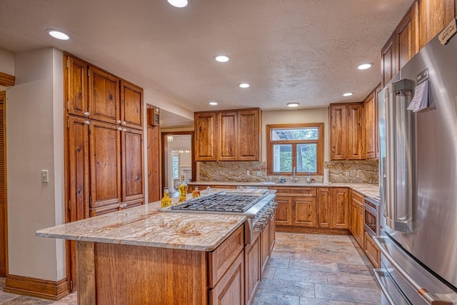kitchen with a center island, backsplash, sink, appliances with stainless steel finishes, and light stone counters