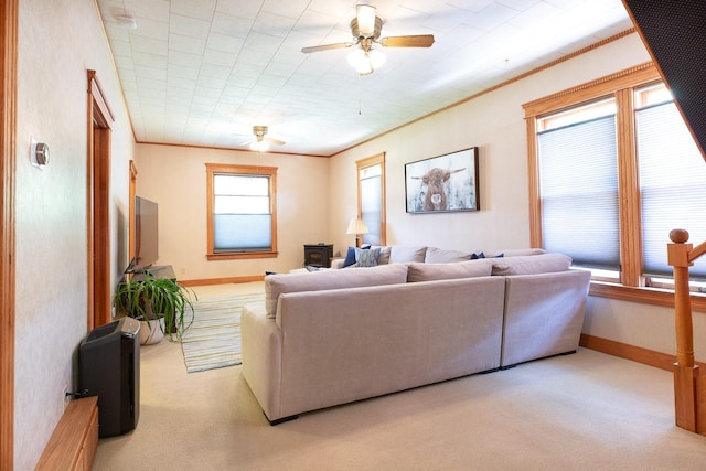 carpeted living room featuring a wood stove, ceiling fan, and ornamental molding