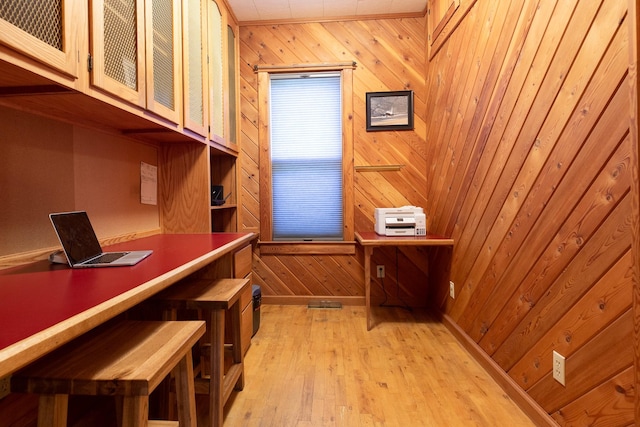 wine area with wood walls, light wood-type flooring, and built in desk