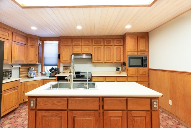 kitchen with black microwave, wooden walls, sink, and an island with sink