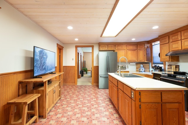 kitchen featuring sink, black range with electric cooktop, stainless steel fridge, an island with sink, and wood ceiling