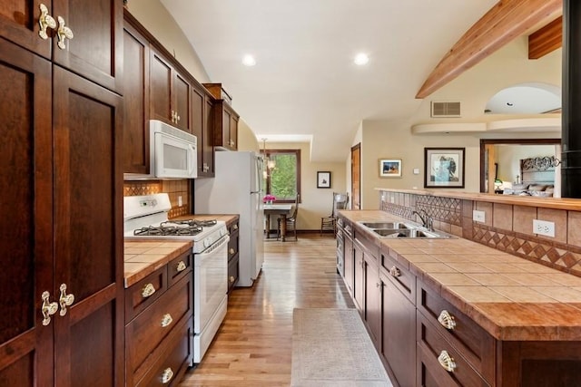 kitchen featuring decorative backsplash, white appliances, sink, light hardwood / wood-style flooring, and tile counters