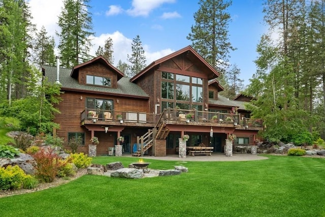 rear view of property featuring a patio, a fire pit, a lawn, and a wooden deck