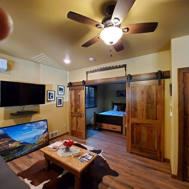 interior space featuring an AC wall unit, a barn door, ceiling fan, and wood-type flooring