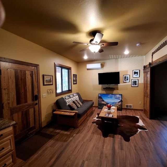 living room featuring a barn door, ceiling fan, a wall mounted air conditioner, and dark hardwood / wood-style floors