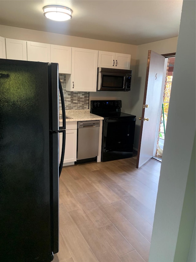 kitchen with decorative backsplash, light wood-type flooring, light stone counters, black appliances, and white cabinetry